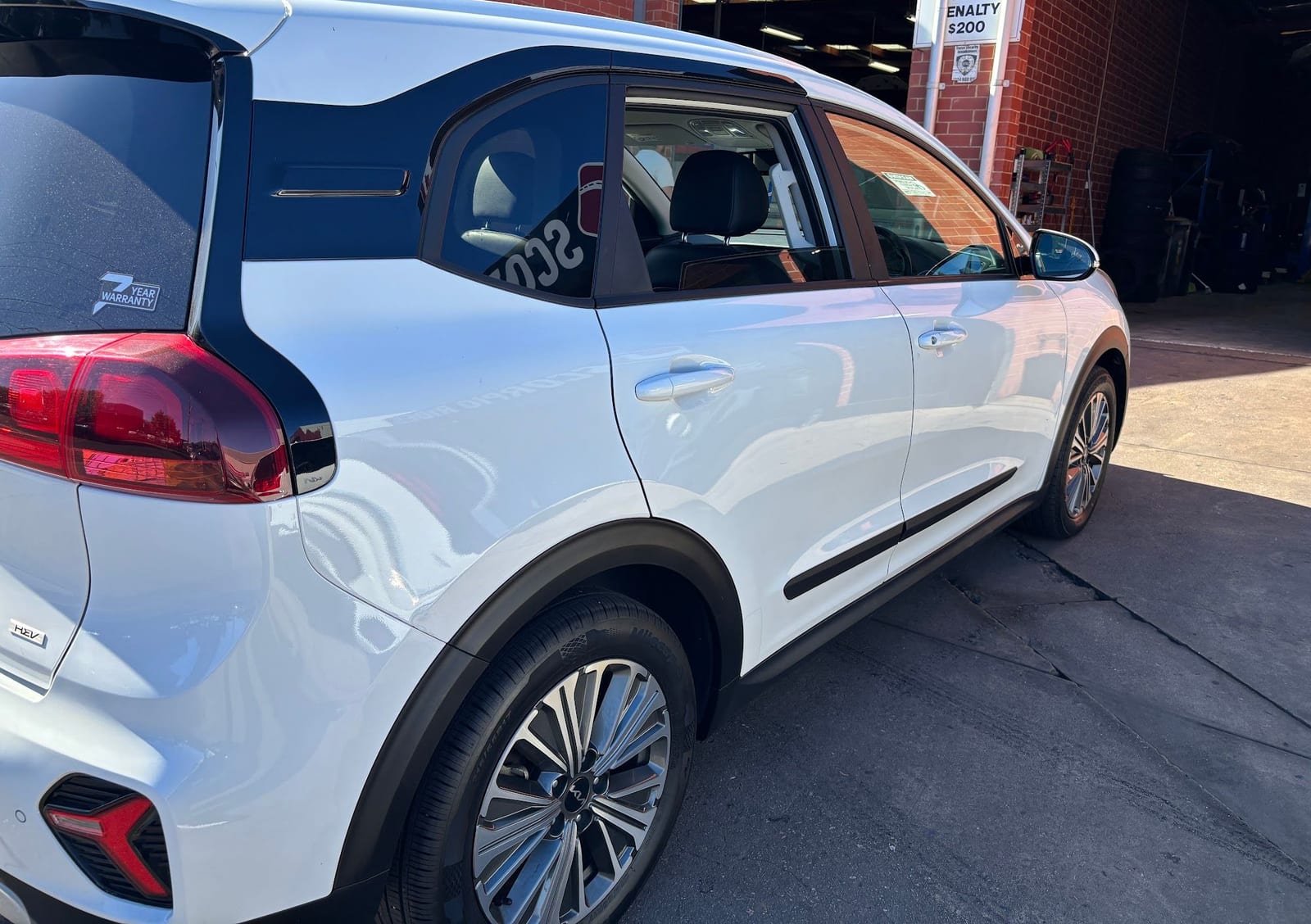 The rear corner of a white Kia SUV outside a brick workshop building